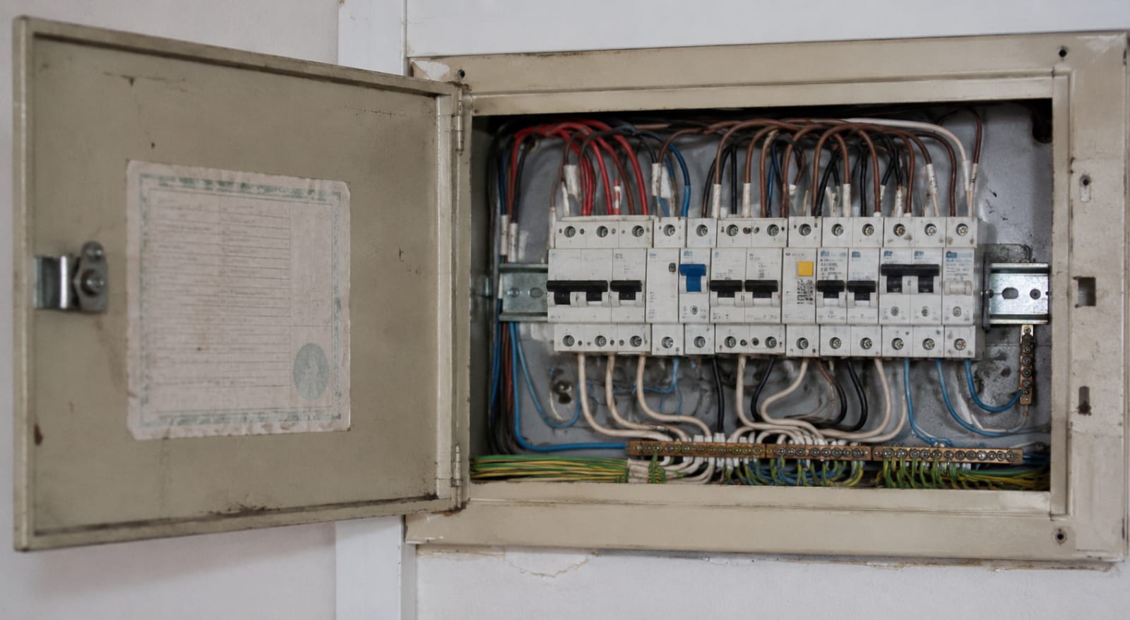 An open residential distribution board with an ageing compliance sticker inside the panel door.