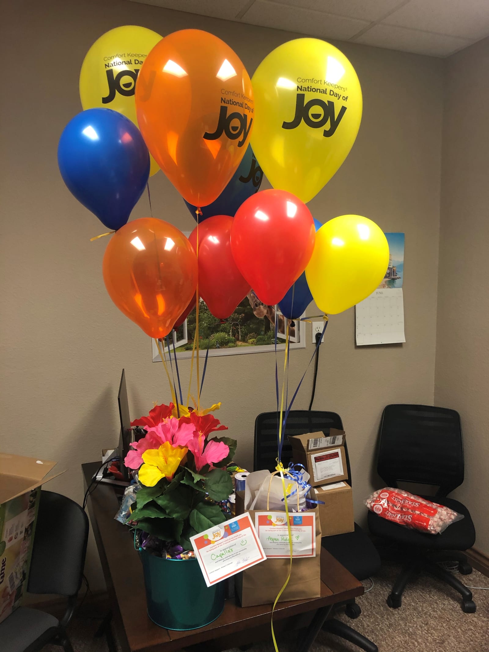 A flower arrangement and National Day of Joy balloons on an office desk