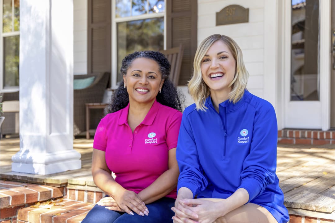 Two Comfort Keepers caregivers sitting together on the front steps of a house