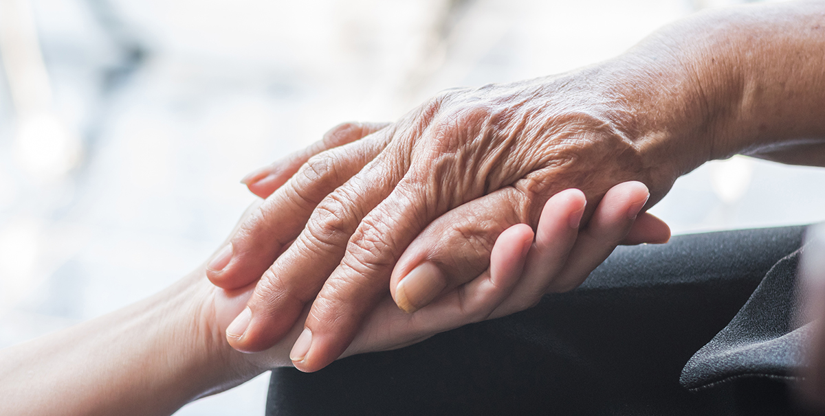 A young caregiver from Comfort Keepers' hand compassionately clasps the hand of a senior aged client.