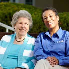 Senior and caregiver sitting outside on a sunny day smiling for camera