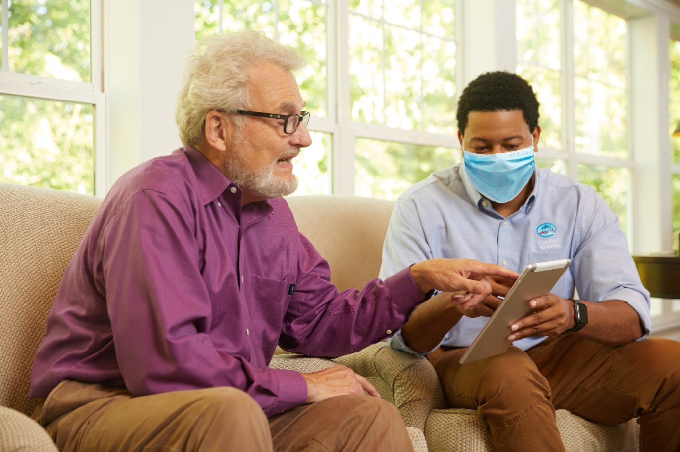 Senior and Comfort Keepers Caregiver in surgical mask touching an iPad tablet