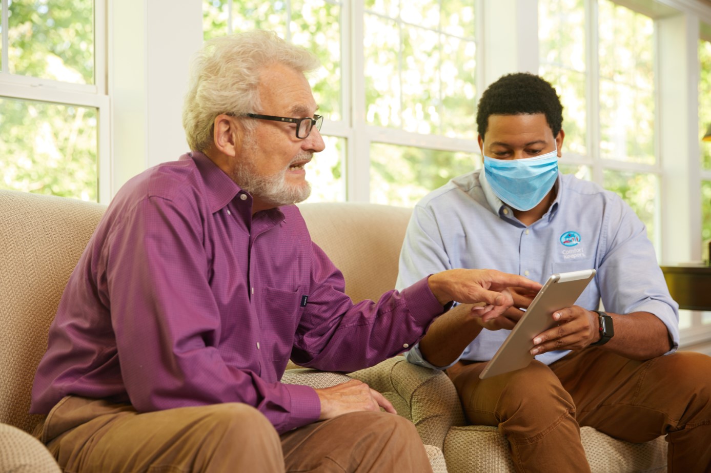 Senior male and male Comfort Keepers Caregiver looking at electronic tablet device.