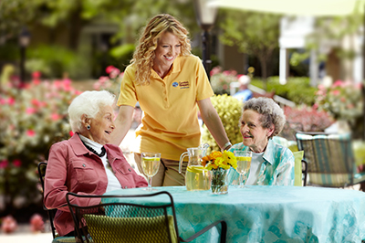 two seniors at table with caregiver in yellow shirt drinking lemonade outside oakdale