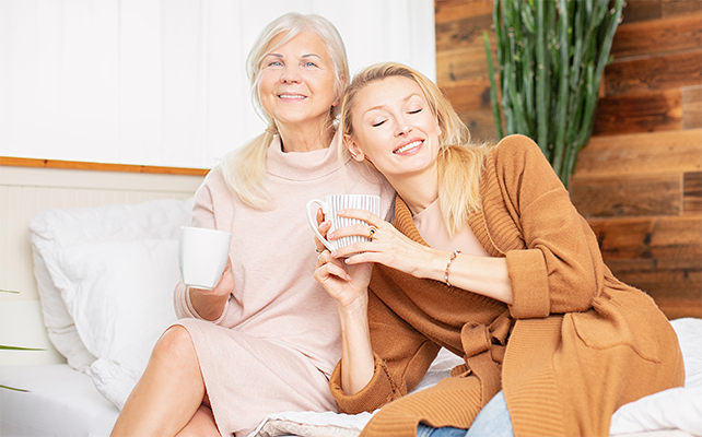 Woman and her granddaughter talking and drinking coffee, sitting on bed at home.