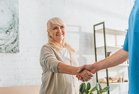 Smiling senior woman and young caregiver shaking hands