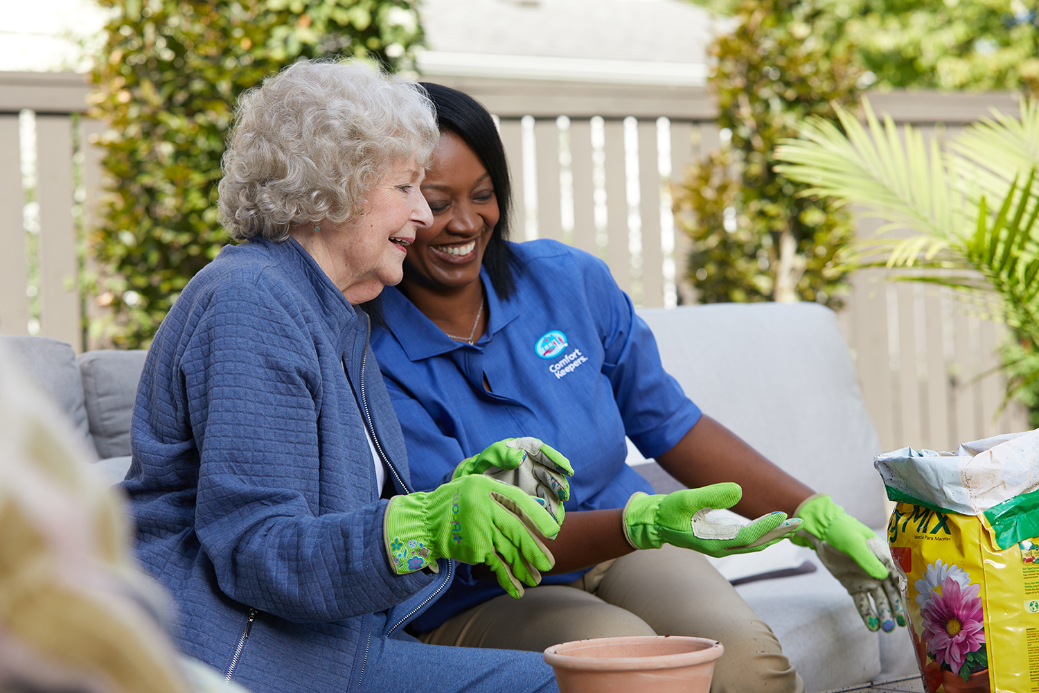 Senior woman and Comfort Keepers Caregiver planting flowers on a patio