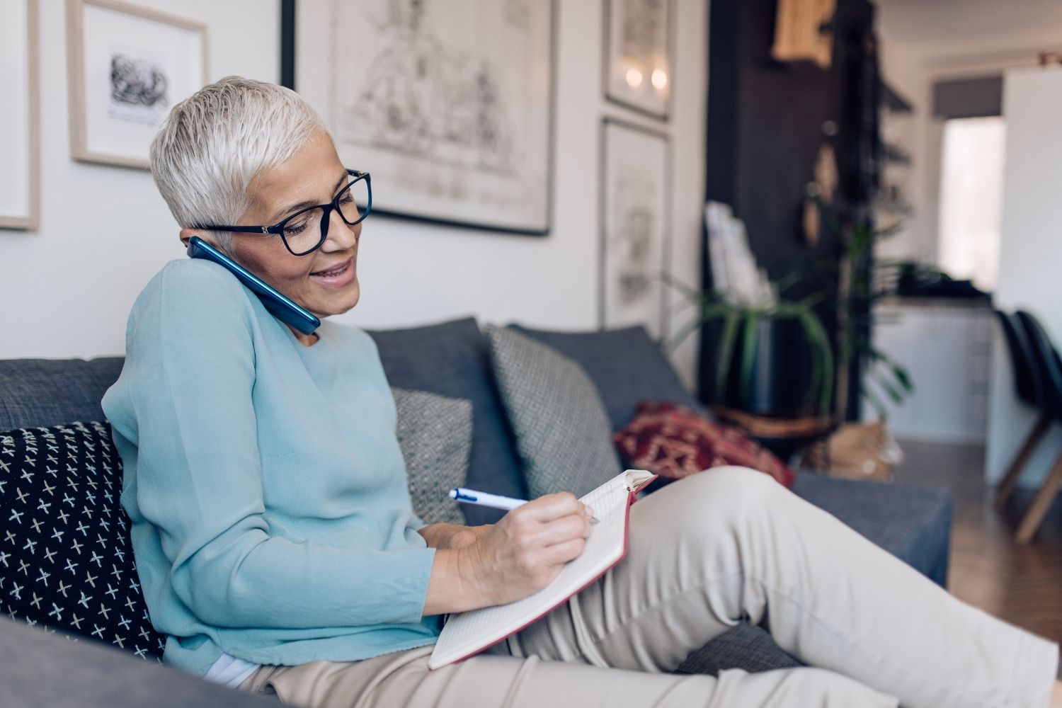 Older woman taking notes and talking on a cellular phone.