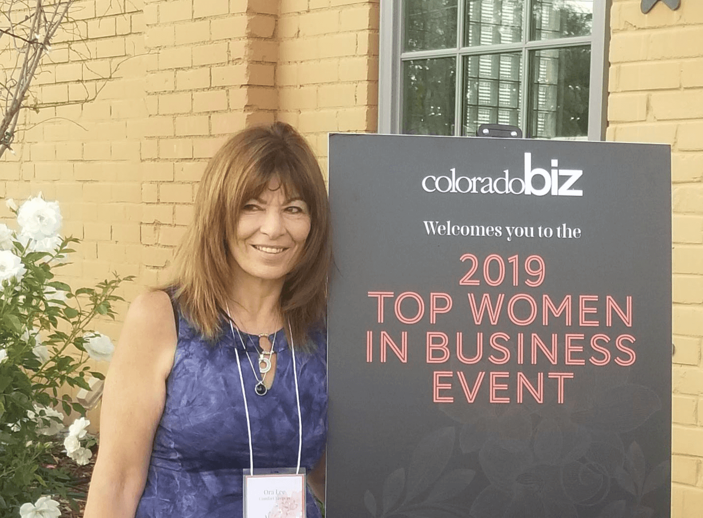 Comfort Keepers Owner, Ora Lee, standing next to sign that says 2019 Top Women In Business Event