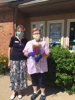 Two women wearing masks in front of the Comfort Keepers office holding bouquet of flowers