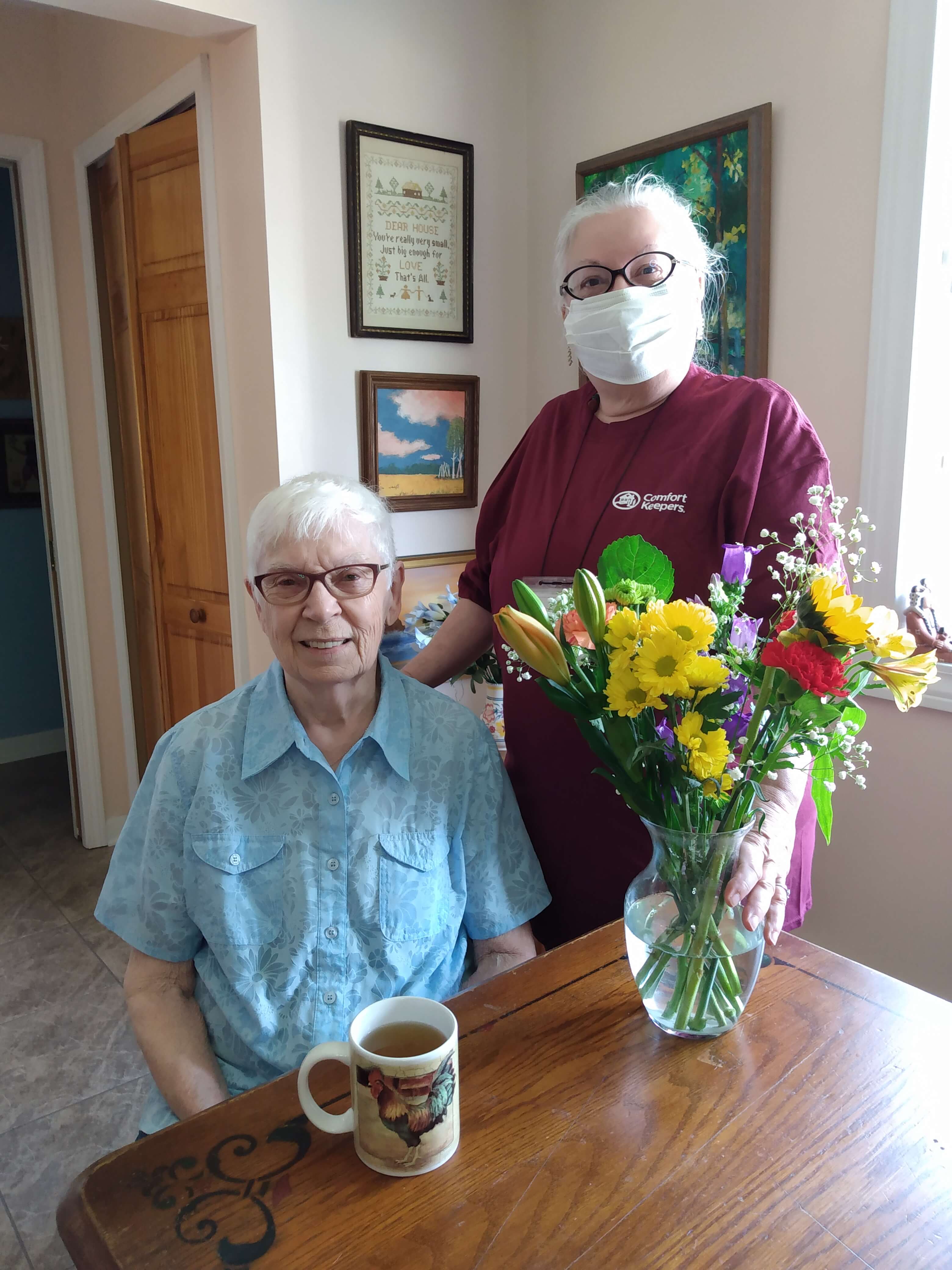 Caregiver and senior smiling for the camera next to a vase of flowers