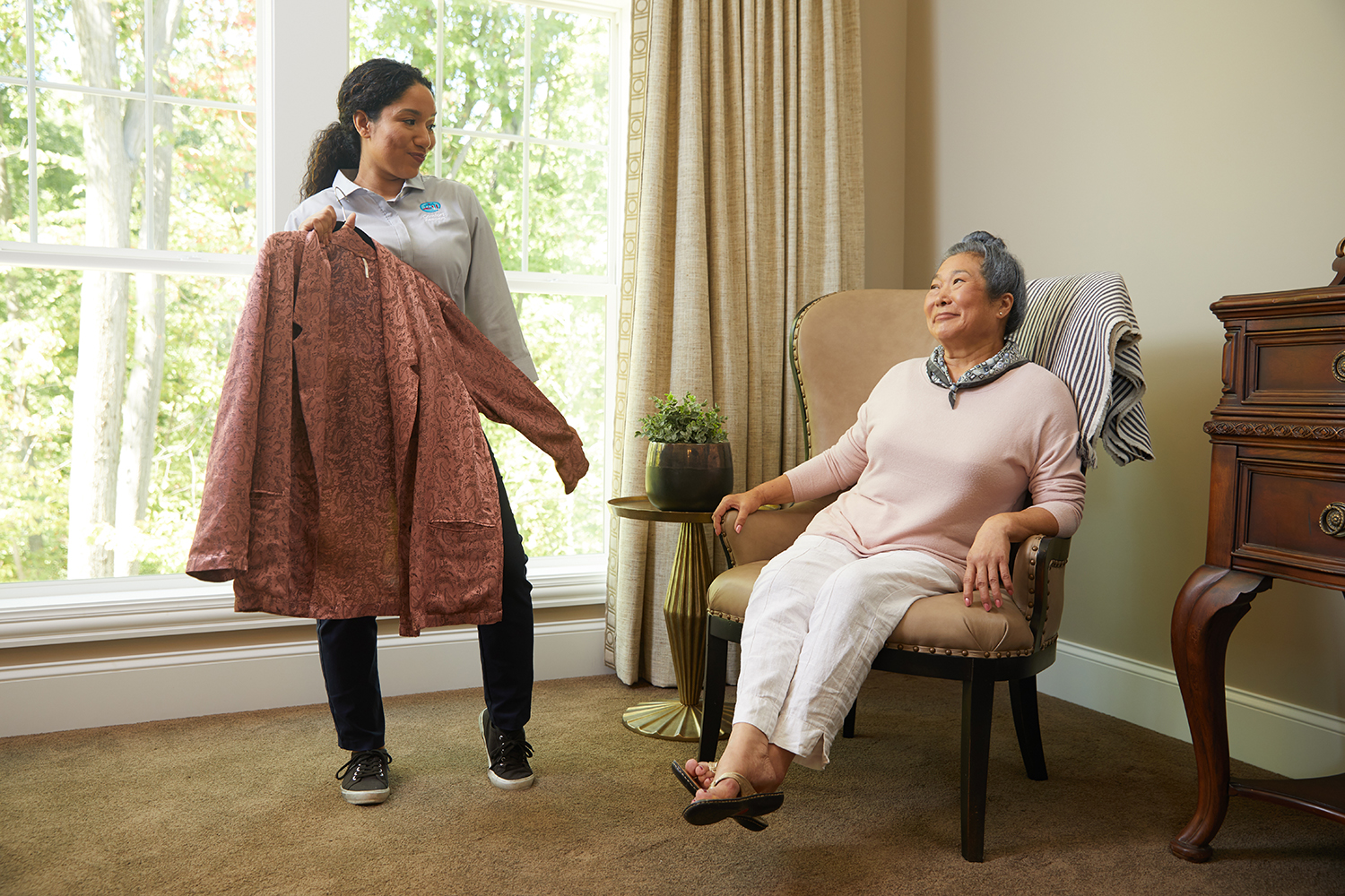 Comfort Keepers caregiver holding a long jacket for seated older woman