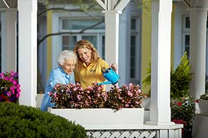 Senior and caregiver watering flowers in flowerbox on porch