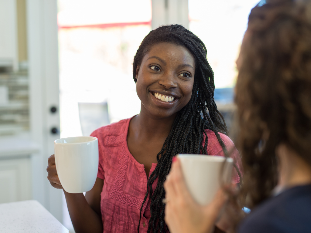 Woman smiling toward a friend and holding a white coffee mug