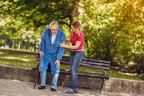 Caregiver helping senior stand up in westminster park