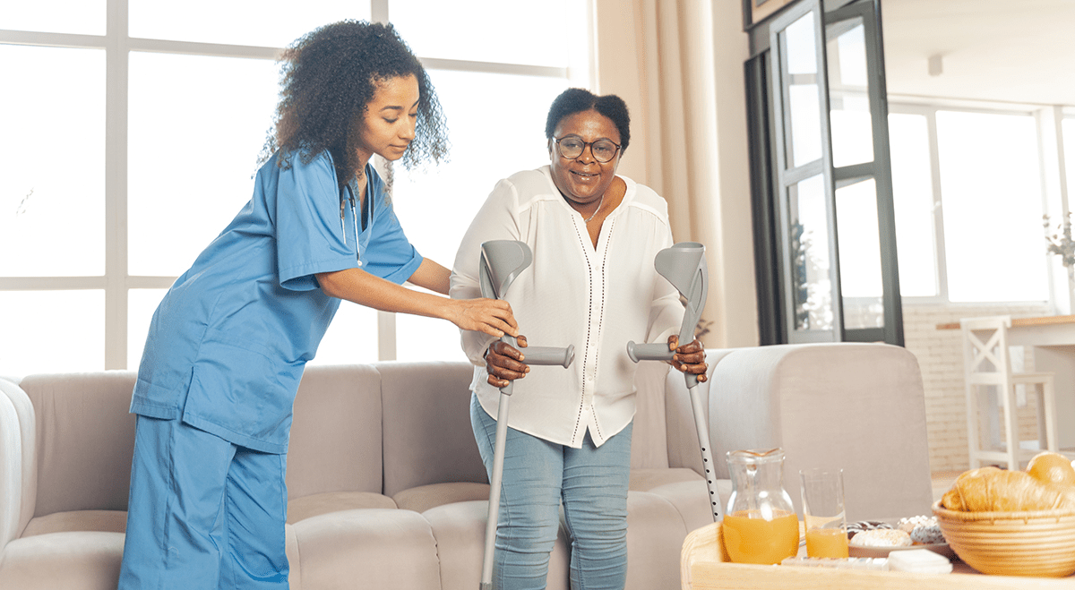 a caregiver helping senior walk with crutches