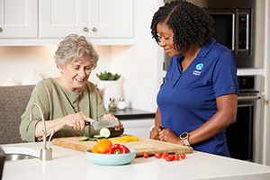 Caregiver and senior with dementia preparing a salad together in kitchen