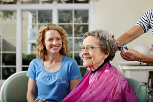 Caregiver sitting with senior as senior gets a hair cut at salon