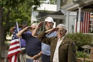 three veterans standing outside home holding flag and saluting