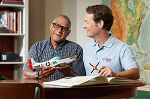 Senior with dementia and his companion caregivers looking at a model airplane