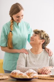 senior sitting at table with senior companion standing behind her and hands on senior's shoulders