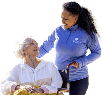 Caregiver looking down warmly at their client while pushing them in a wheelchair during an outdoor walk