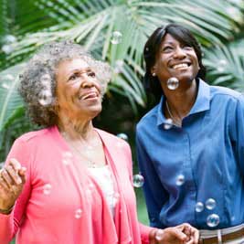 A senior woman and her caregiver smiling at bubbles, enjoying 24-hour in-home care services from Comfort Keepers.