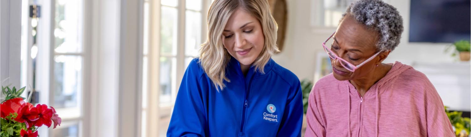 A caregiver assisting a client with a writing task that is out of frame.