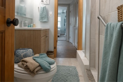 Non-slip socks, clean clothing, and toiletries set beside a walk-in shower in a compact home bathroom for a safer senior morning routine.