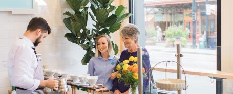 2024 National Day of Joy 2 Women ordering a drink at a bistro from a male barista