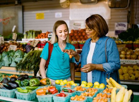 Caregiver and senior looking at peppers in the produce section of a grocery store.