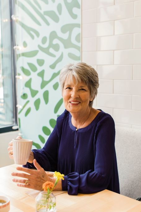 Photo of senior woman smiling at the camera while drinking a coffee