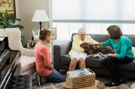 Senior and her two daughters sitting on a couch petting a dog