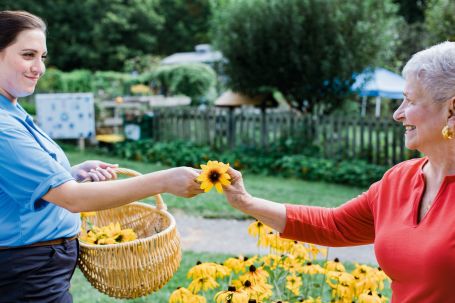 Caregiver holding a basket of sunflowers and handing on to a senior