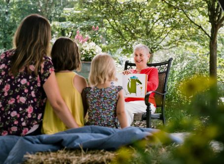 Senior reading a picture book with her grandchildren outside