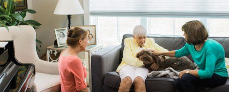 Senior and her two daughters sitting on a couch petting a dog