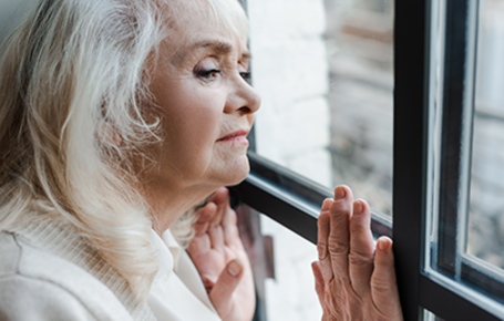 isolated and upset senior standing near window during quarantine