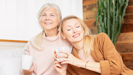 Woman and her granddaughter talking and drinking coffee, sitting on bed at home.