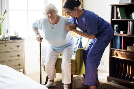 female care taker helping elderly woman up from her chair 