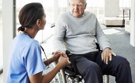 caregiver holding hand of senior man sitting in a wheel chair 