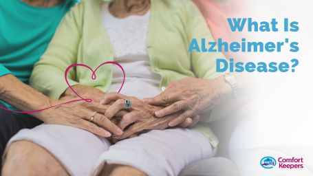 Older woman sitting with hands held together loosly in lap, she is surrounded by 2 people beside her, each holding out one hand- touching her hands. Image caption reads, "What is Alzheimers Disease"