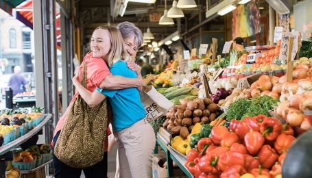 A Comfort Keeper gives a hug in grocery store while standing in front of produce display