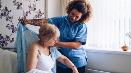 Caregiver helping senior woman get dressed. 