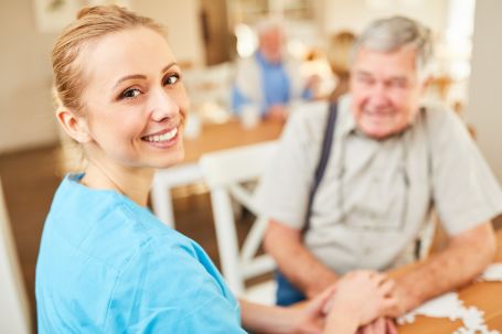 Smiling female caregiver with senior man in background 