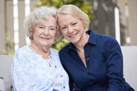 Senior with daughter sitting outside at home and smiling at camera