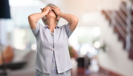 Frustrated family caregiver with hands on head at bottom of stairs in her parents home