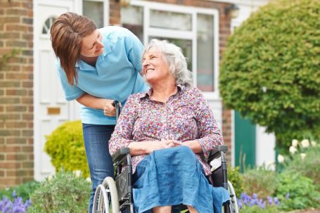 Woman caregiver pushing elderly lady in wheelchair.