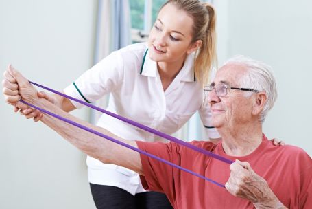 A caregiver helping a senior man exercise. 