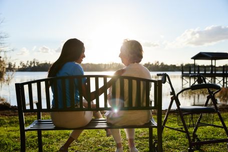caregiver and senior sitting on a bench in front of the lake