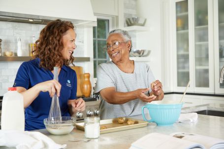 Senior woman having a joyful moment with Comfort Keepers caregiver, preparing cookies and sharing a laugh.